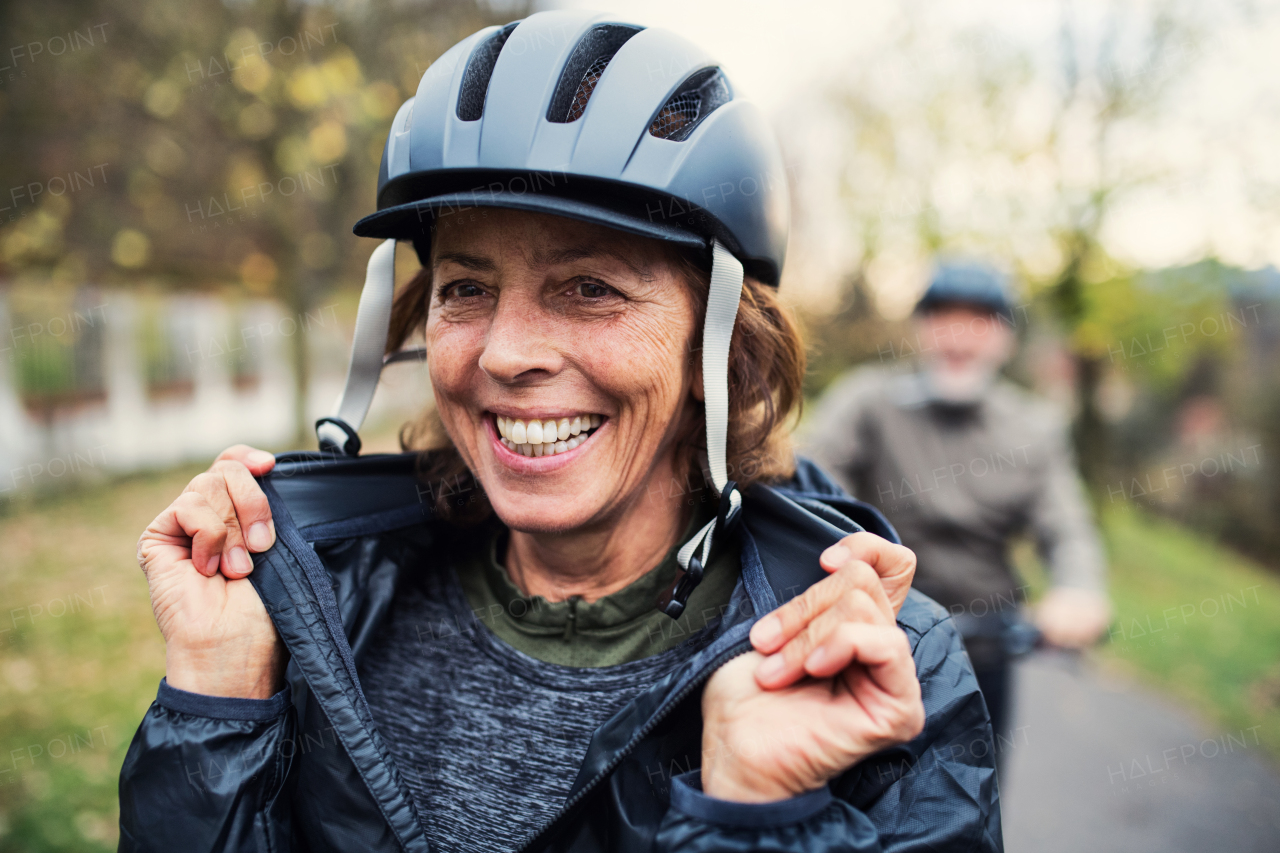 An active senior couple with helmets and electrobikes standing outdoors on a road in park.