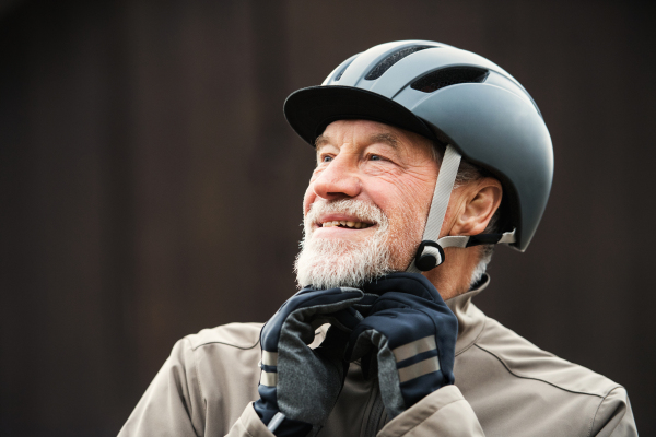 An active cheerful senior man standing outdoors in town, putting on a bike helmet.