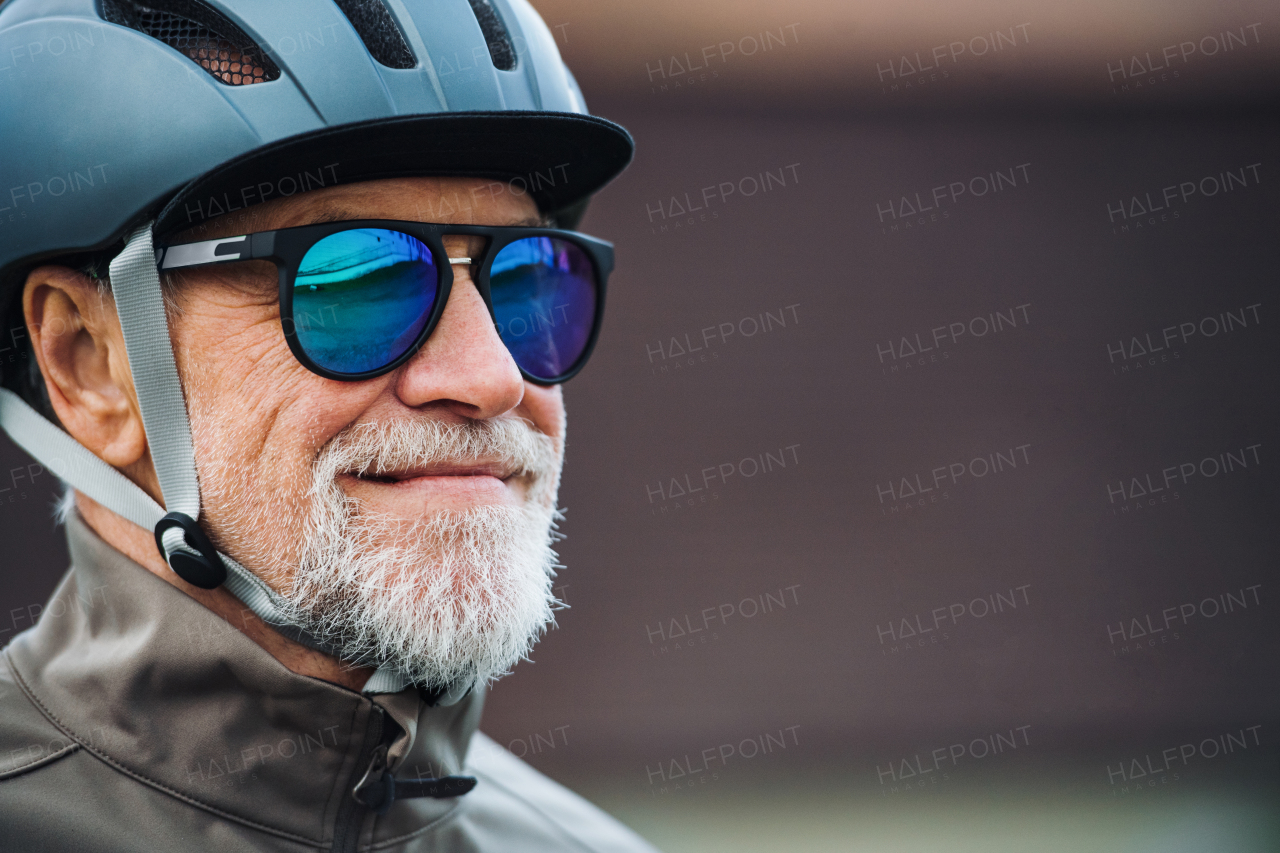 Close-up of active senior man with sunglasses and bicycle helmet standing outdoors. Copy space.
