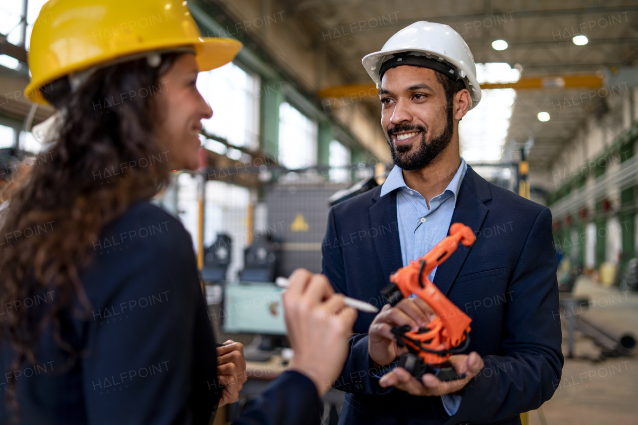 A man engineer holding model of industrial robotic arm and showing to collegue in factory.