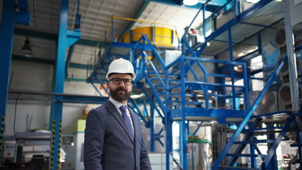 A chief Engineer in the hard hat walks through industrial factory while holding tablet.