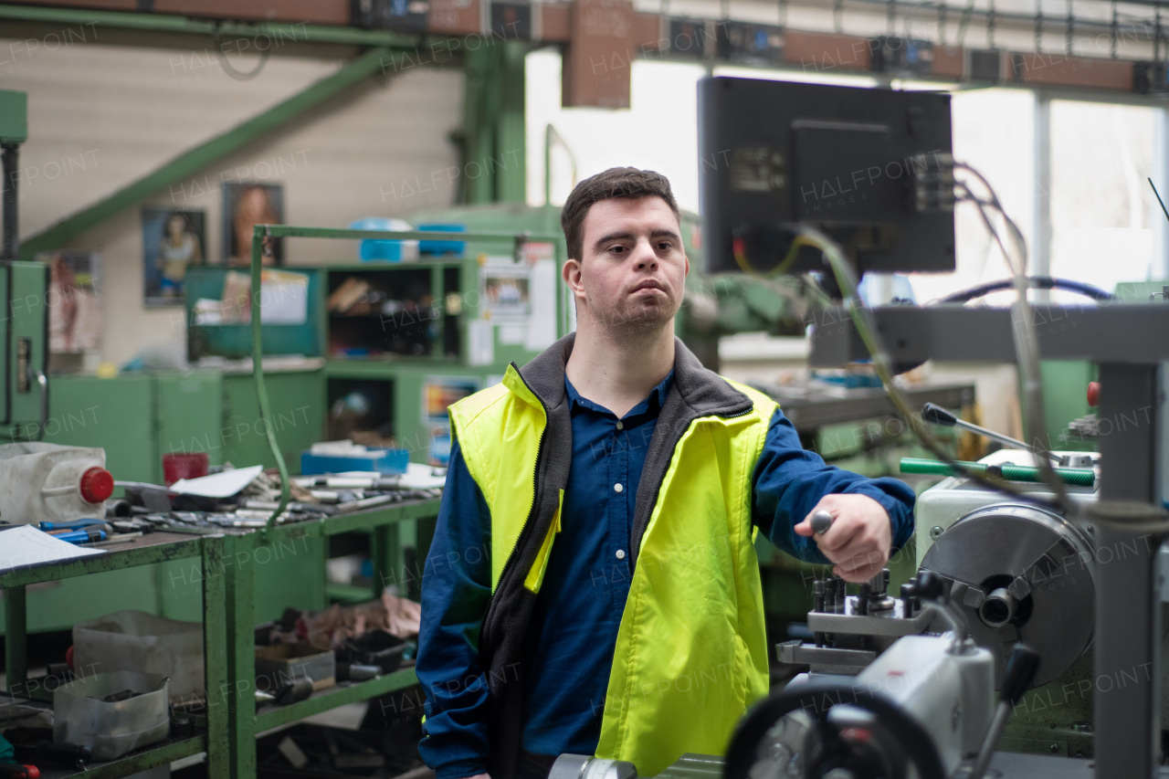 A young man with Down syndrome working in industrial factory, social integration concept.