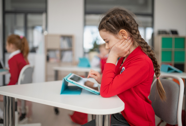 A bored schoolgirl using digital tablet during lesson in classroom at primary school.