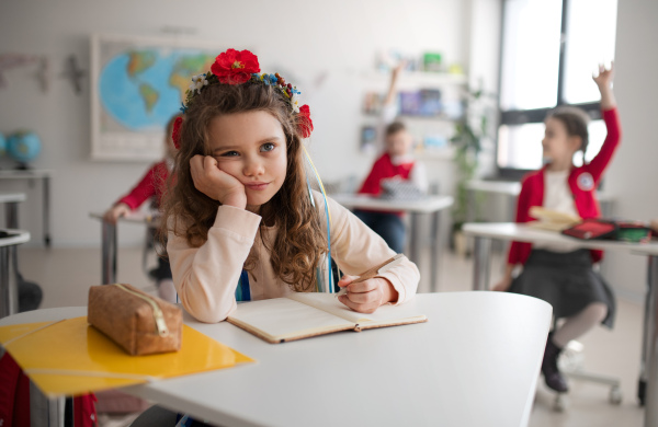 A little sad Ukrainian girl sitting in classroom during class, concept of enrolling Ukrainian kids to schools.