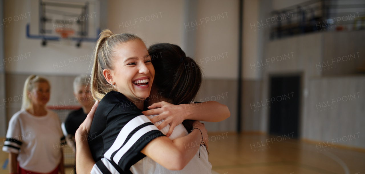 A group of young and old women, sports team players, in gym celebrating victory, hugging.