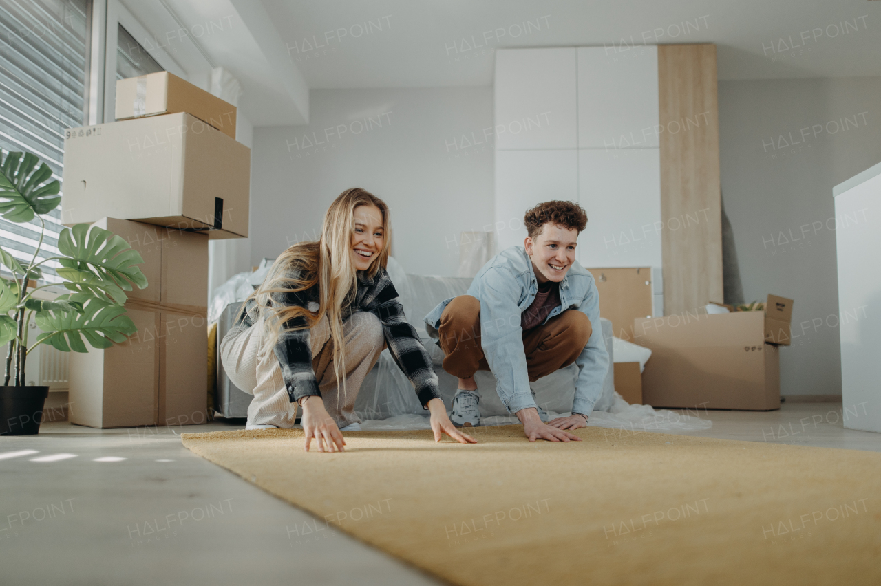 A cheerful young couple in their new apartment, rolling out carpet. Conception of moving.
