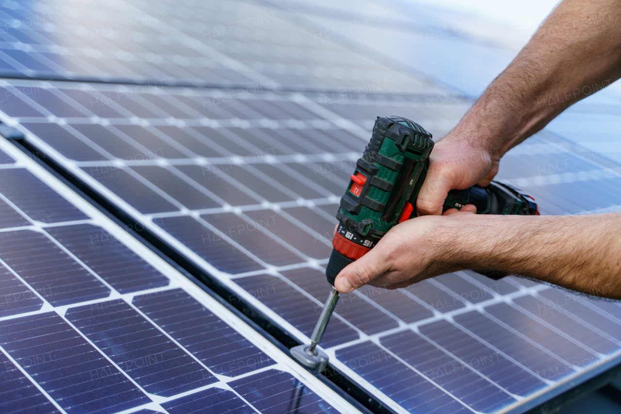 A man worker installing solar photovoltaic panels on roof, alternative energy concept. Close up hands with drill.