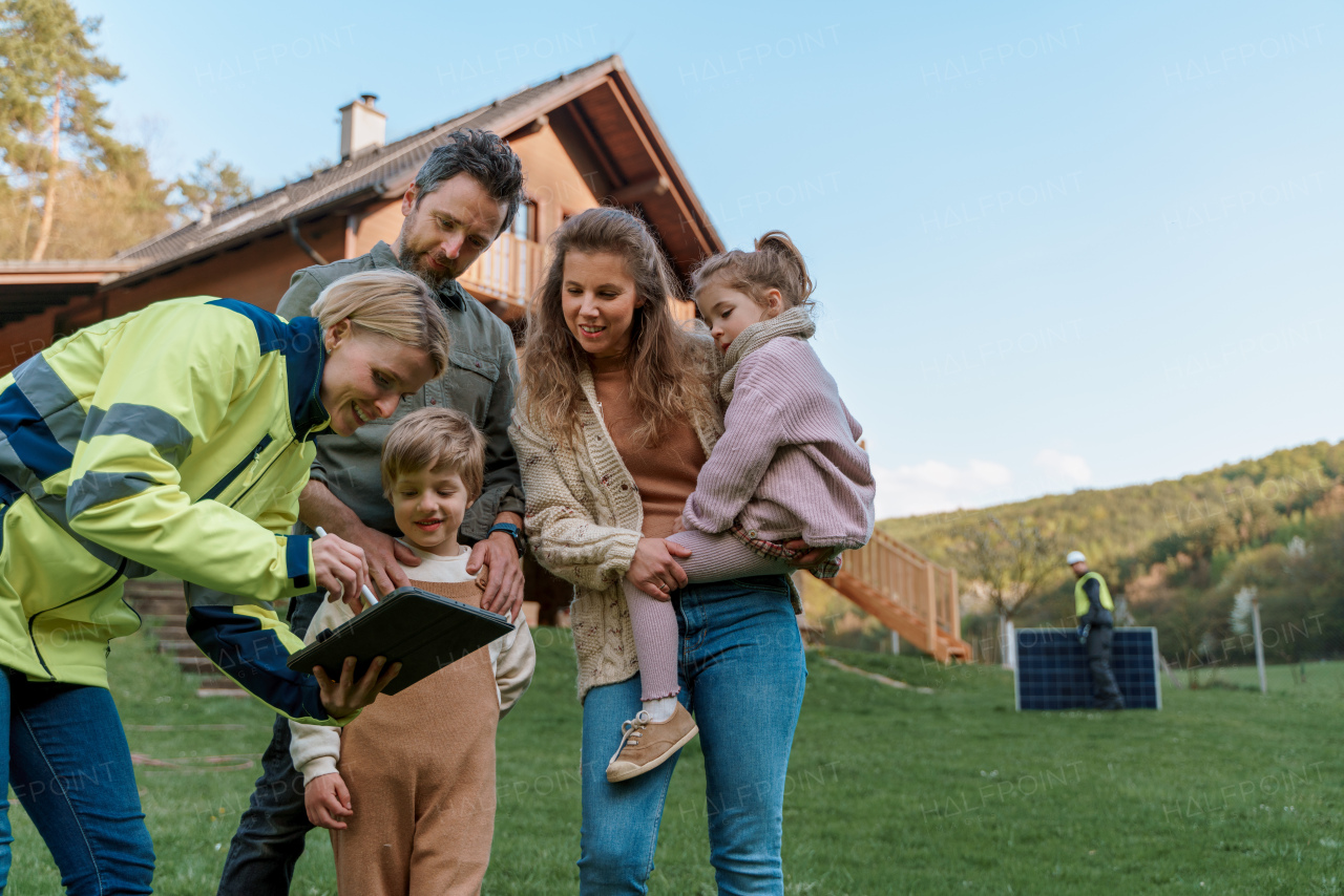 A woman engineer talking to young family about solar panel installation in front of their house.