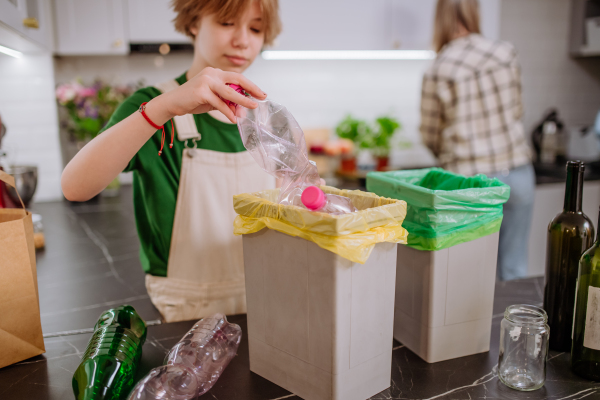 A teen girl throwing plastic bottles in recycling bin in the kitchen.