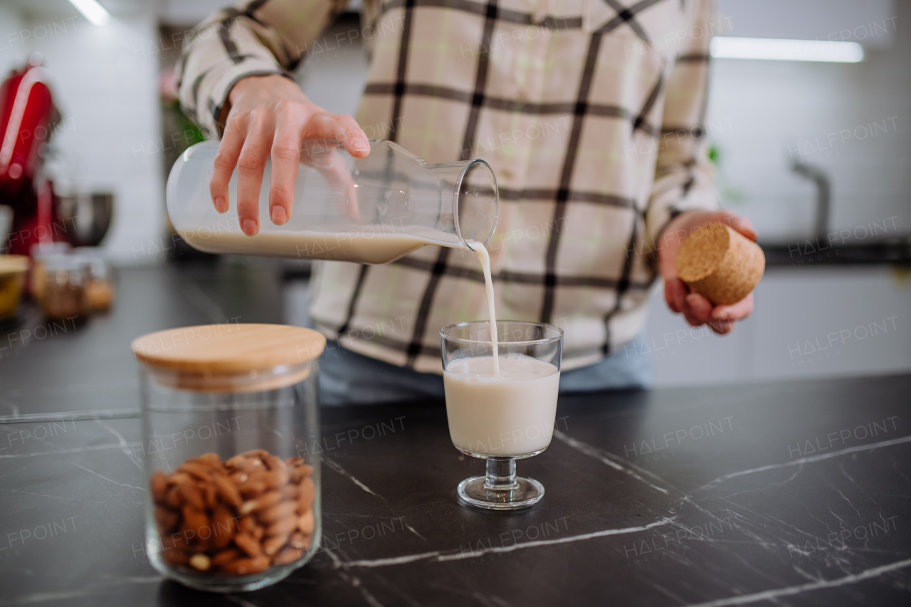 A woman pouring almond milk into a glass in kitchen. Healthy vegan product concept.