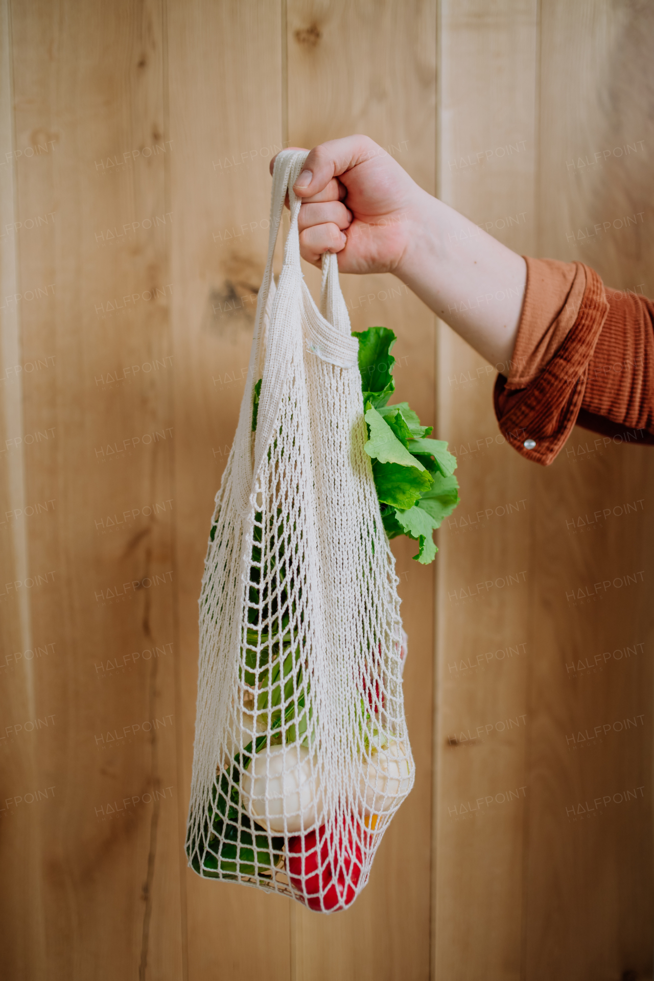 A woman holding a reusable mesh bag with fresh vegetables. Zero waste concept.