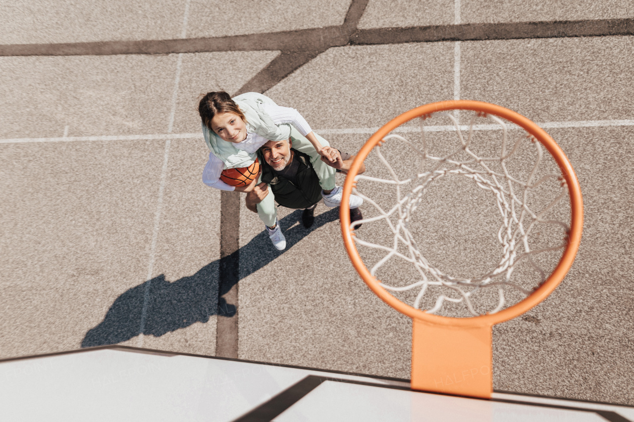 A father and teenage daughter playing basketball outside at court, high angle view above hoop net.