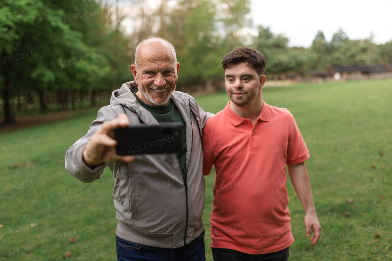 A happy senior father with his young son with Down syndrome taking selfie in park.