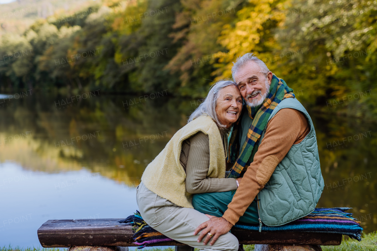 Senior couple in love sitting together on a bench near lake, during autumn day.