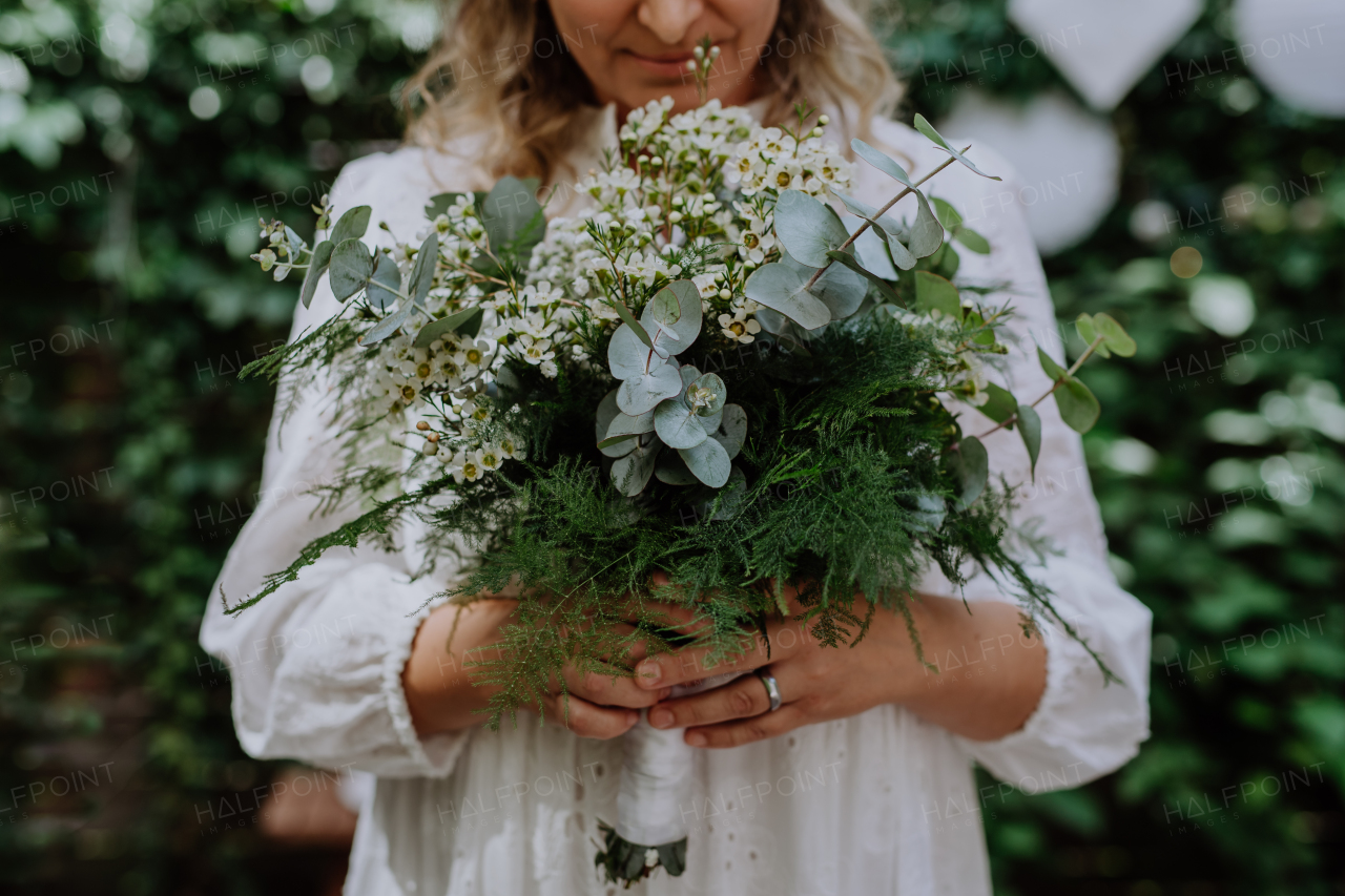 A close-up ofwedding bouquet in bride's hands at reception outside in backyard