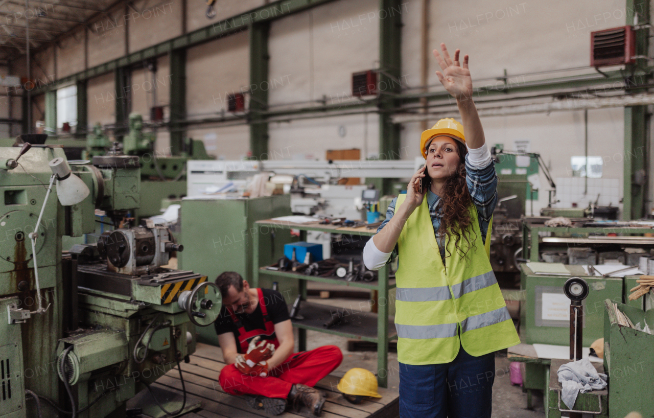 A woman is calling ambulance for her colleague after accident in factory. First aid support on workplace concept.