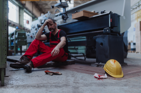 A eorker suffering from pain after accident in factory. First aid support on workplace concept.