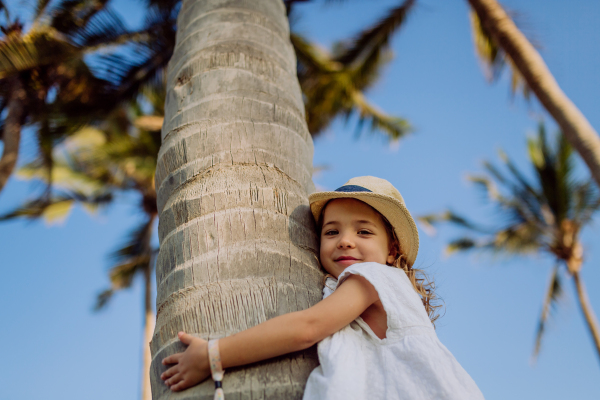 Happy little girl hugging palm tree during the tropical vacation.