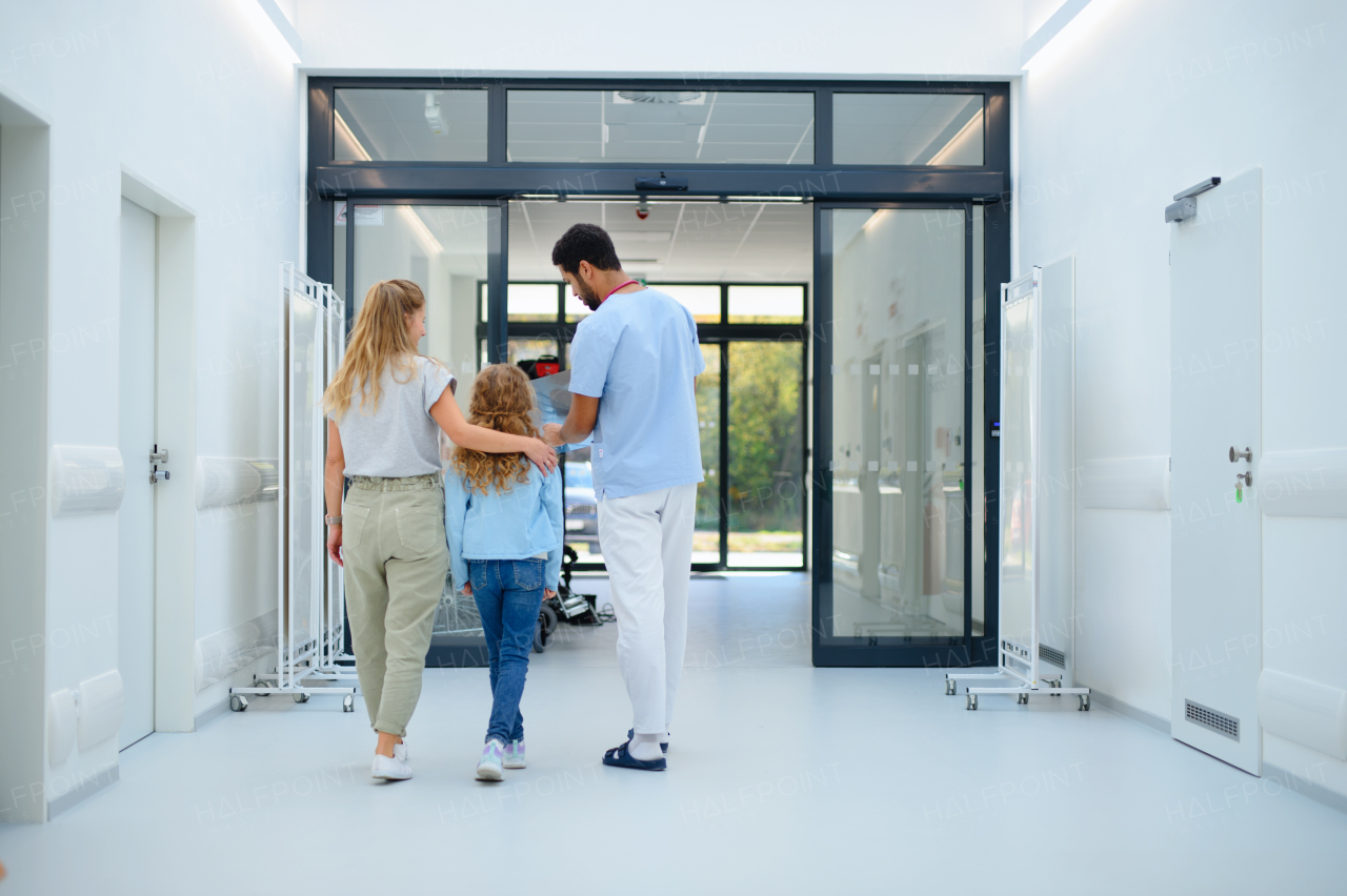 Rear view of young multiracial doctor talking with mother and little girl at hospital corridor,showing them a x-ray image.