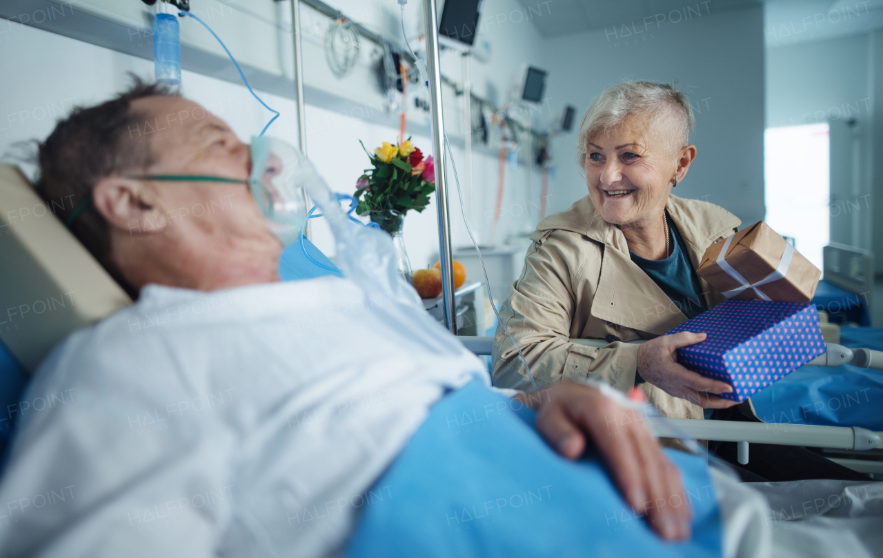 Senior woman visiting her husband in hospital, bringing him gifts.