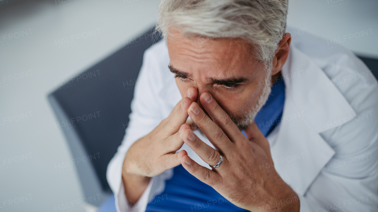 Portrait of frustrated, exhausted doctor sitting in hospital corridor, crying. Concept of burnout syndrome among doctors, health care workers.