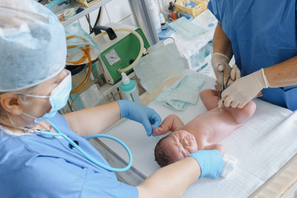 Neonatal nursers, doctor examining newborn baby, taking care of infant after birth. Cutting umbilical cord. Neonatal care, newborn's health and well-being.