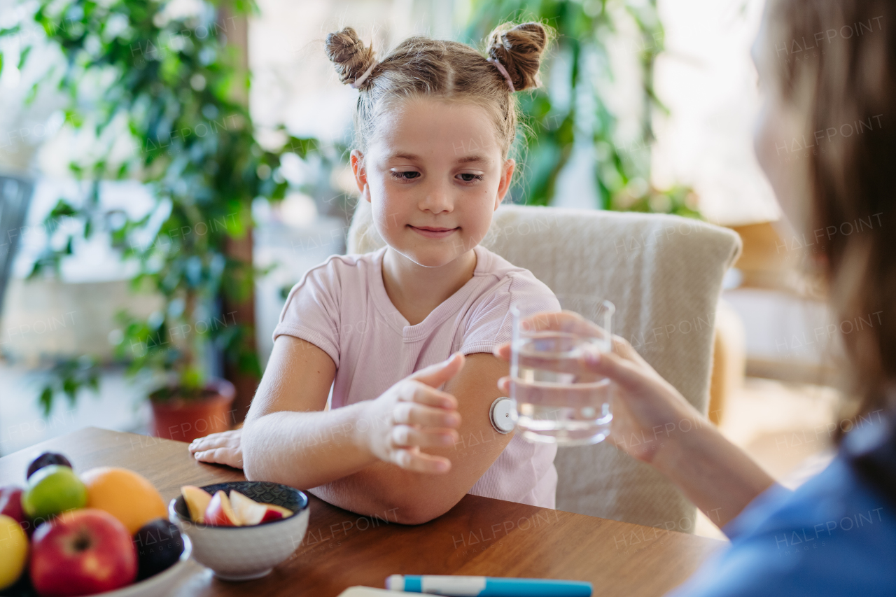 Diabetic girl drinking water to better manage her diabetes. Continuous glucose monitor sensor on diabetic girl's arm.