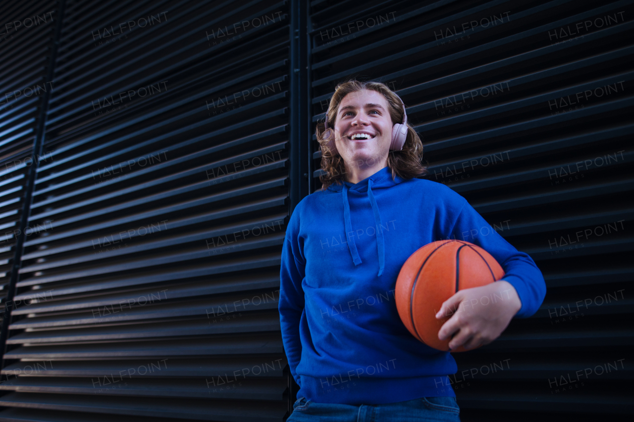 Portrait of young man with headphones holding basketball ball,outdoor in a city. Youth culture.