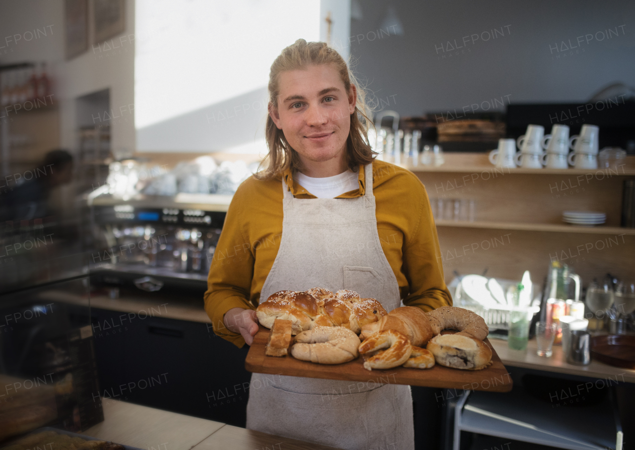 Young man working in a cafe, carring fresh pastries.