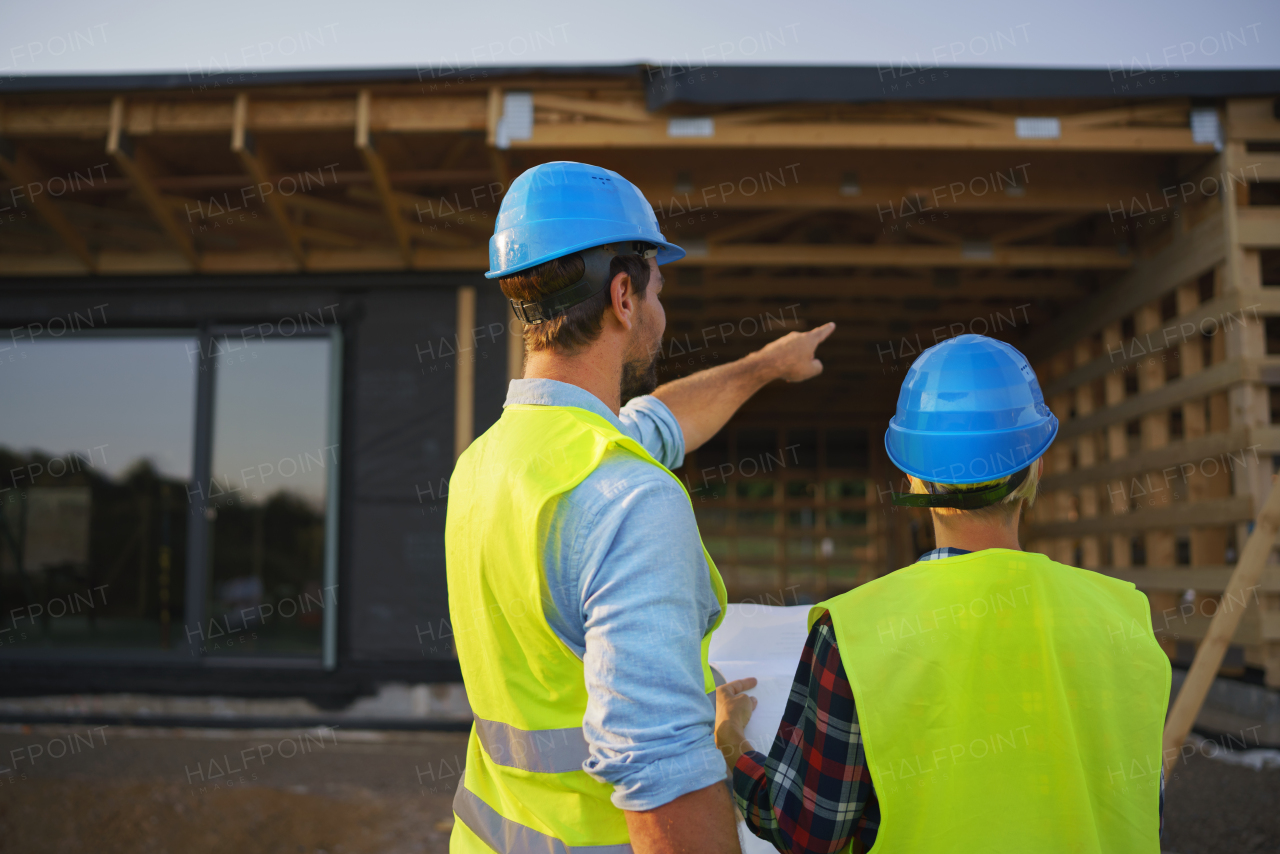Construction engineers or architects with blueprints checking a building site of wood frame house
