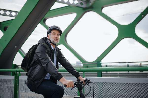 A businessman commuter on the way to work, riding bike over bridge, sustainable lifestyle concept.