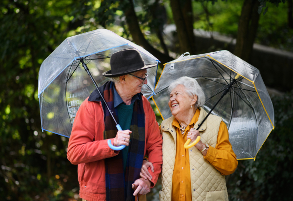 Happy senior couple walking with umbrellas in a park together.