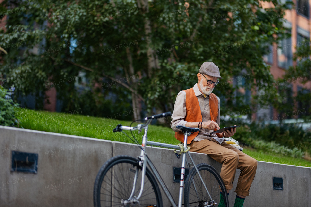 Stylish senior man sitting in the city park, holding tablet, shopping online. Concept of digital literacy, seniors using digital technologies.