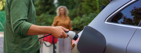 A man holding power supply cable while his wife waiting for car charging at electric vehicle charging station, closeup