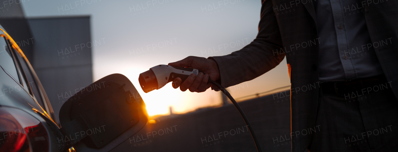 A man holding power supply cable at electric vehicle charging station, closeup