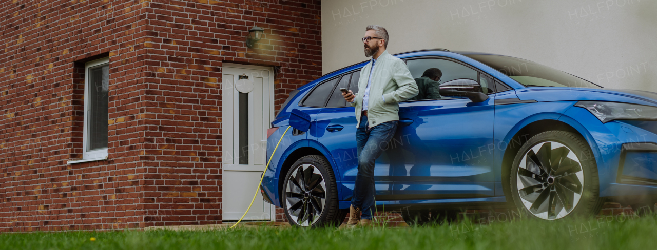 Mature businessman waiting for charging his new electric car.