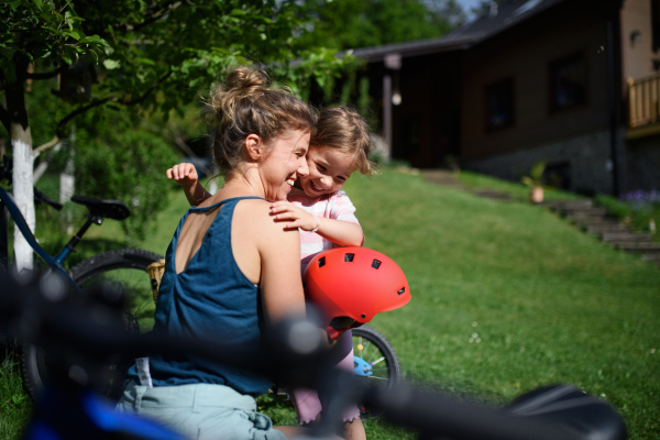 A young mother with little daughter preaparing for bike ride, putting on helmets.