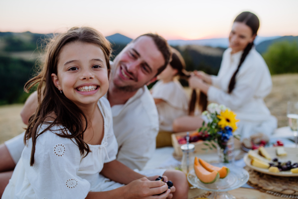 A happy family with children having picnic in park, parents with kids sitting eating healthy meals outdoors.