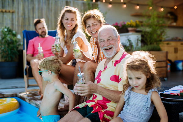 A multi generation family enjoying summer time and sitting at backyard pool.