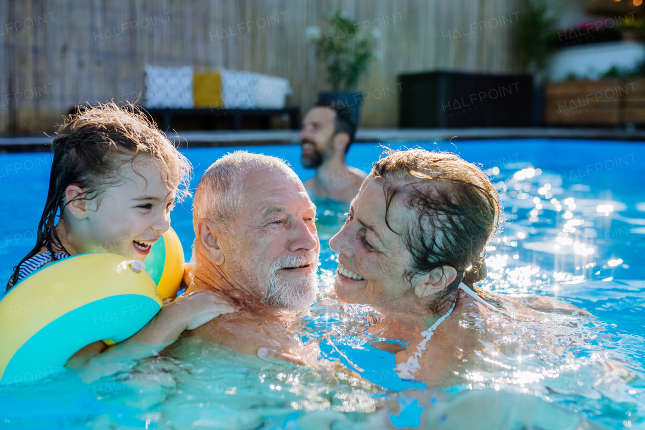 A multi generation family having fun and enjoying swimming in backyard pool.