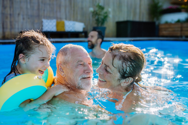 A multi generation family having fun and enjoying swimming in backyard pool.