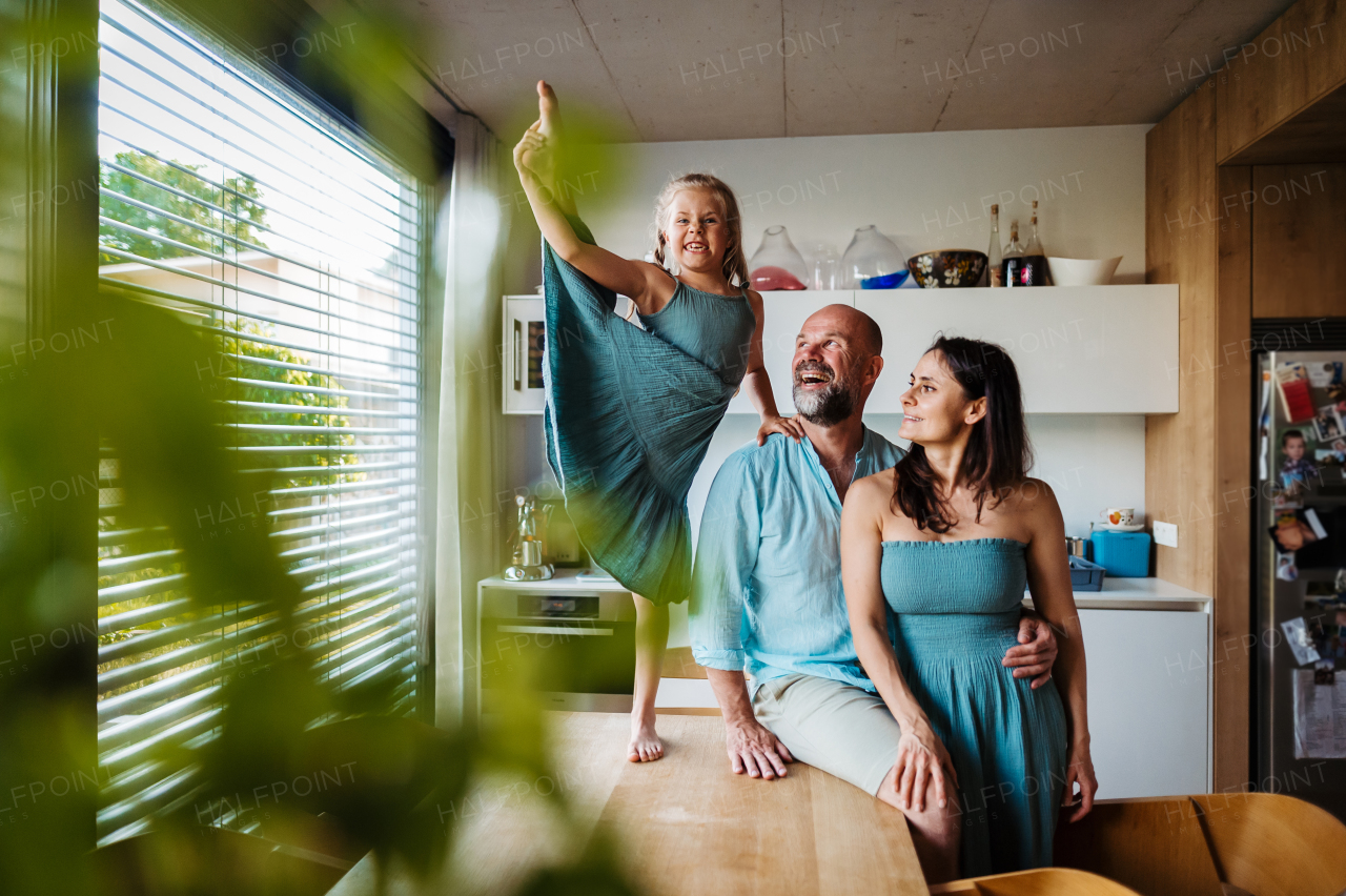 Little girl dancing on the kitchen countertop, while parents watching her. Cheerful family having fun together in kitchen. Little ballerina making funny face. Concept of family bonding.