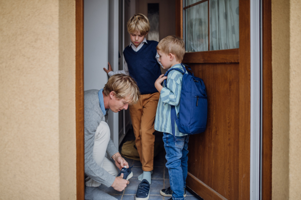 Children getting ready for school, putting on the shoes, getting dressed. Father taking them to school and kindergarten before going to work.