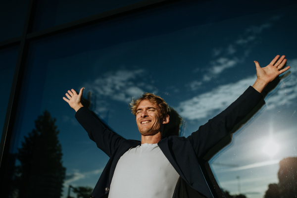 Portrait of handsome mature man with blond hair and closed eyes, standing outdoors in the city, in front of reflective wall.