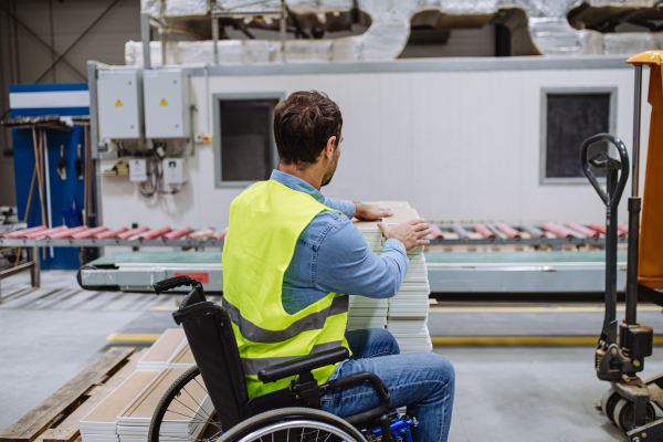 Man in wheelchair working in modern industrial factory, in adjustable workstation. Concept of workers with disabilities, accessible workplace for employees with mobility impairment.