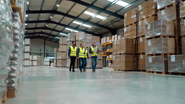 Front view of warehouse workers in reflective vest walking in warehouse. Team of warehouse workers preparing products for shipment.