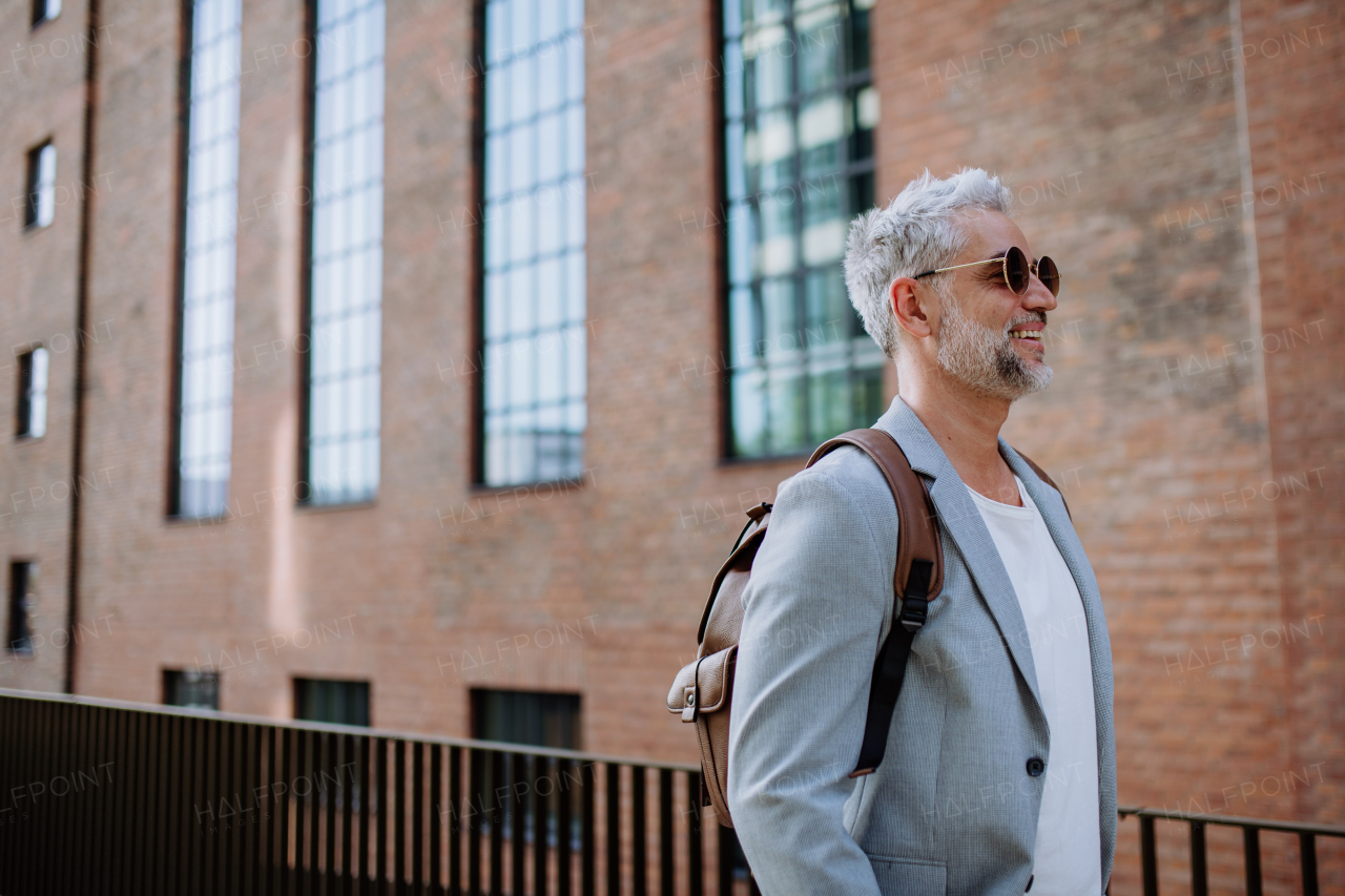 A confident man wearing backpack walking in street, businessman in casual clothes in summer on the way to work.