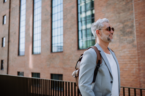 A confident man wearing backpack walking in street, businessman in casual clothes in summer on the way to work.