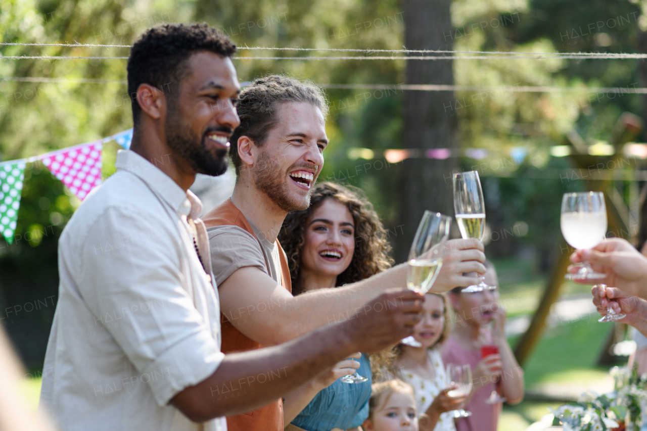 Friends clinking glasses at summer garden party. Celebratory toast at the table. Big family garden bbq.