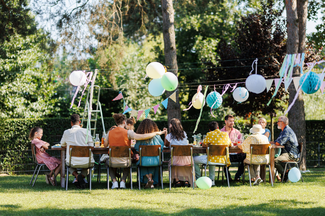 Family and friends sitting at the party table during a summer garden party outdoors. Rear view of people sitting at the table outdoors.